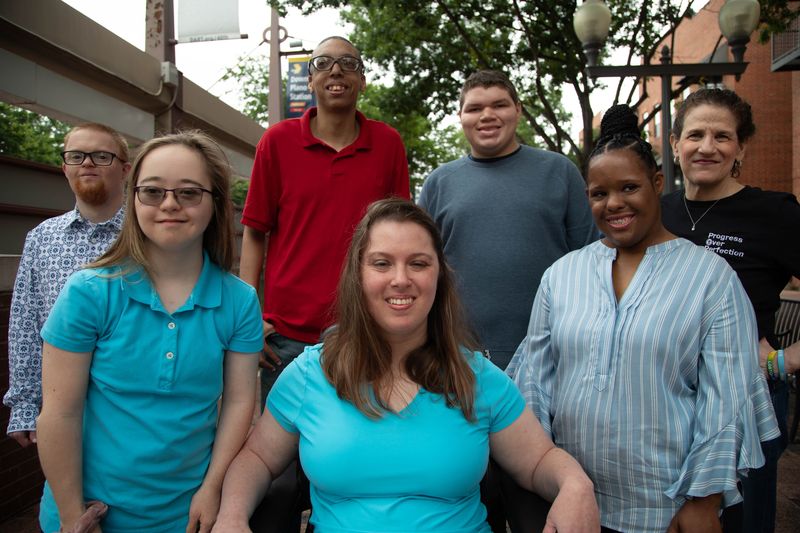 Seven friends and supporters smile together on a downtown plaza.